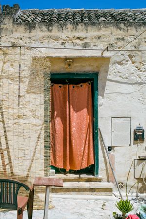 Rustic doorway with orange curtain and green trim against weathered white stone wall.