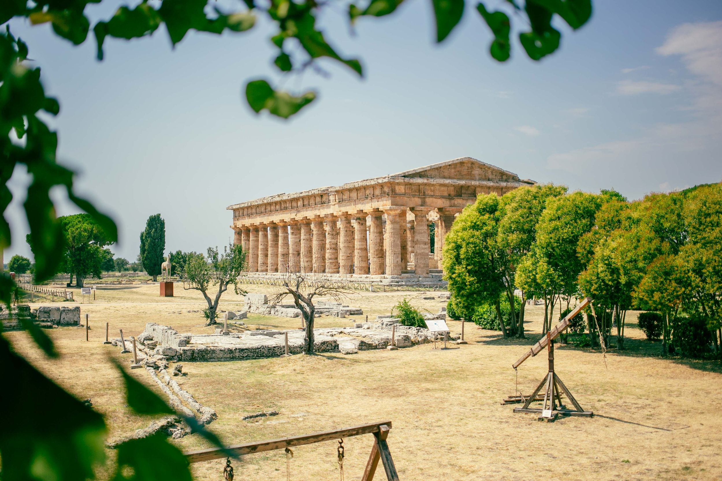 Ancient Greek temple ruins with columns standing against blue sky and green vegetation.