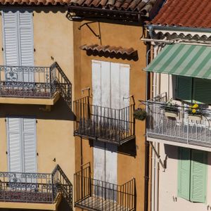 Mediterranean building facade with colorful shutters and wrought iron balconies in sunlight.