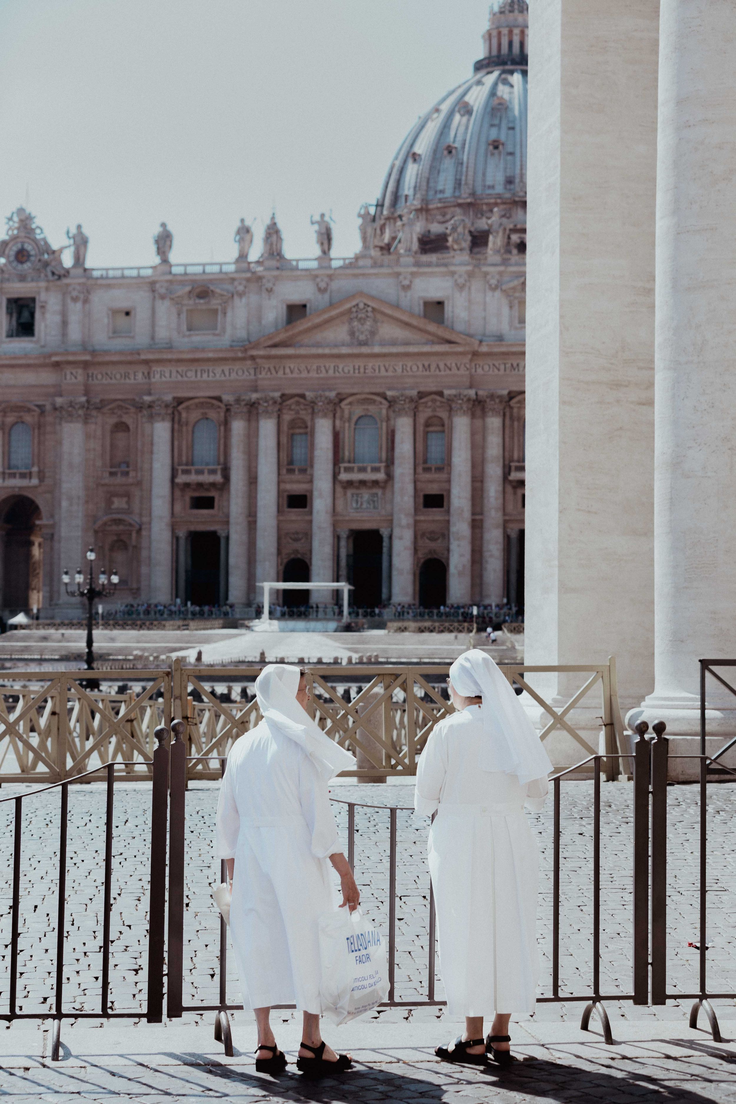 View of St Peter's Basilica dome with religious figures in white robes standing at a railing.