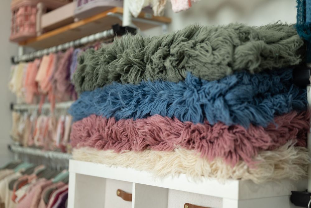 Stacks of soft fluffy blankets in sage green, blue, dusty rose, and cream colors displayed on retail shelving. Marion Indiana