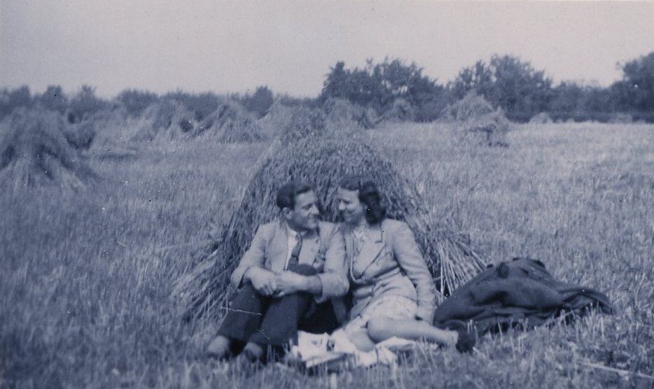 Vintage black and white photograph showing people relaxing against a haystack in a rural field.