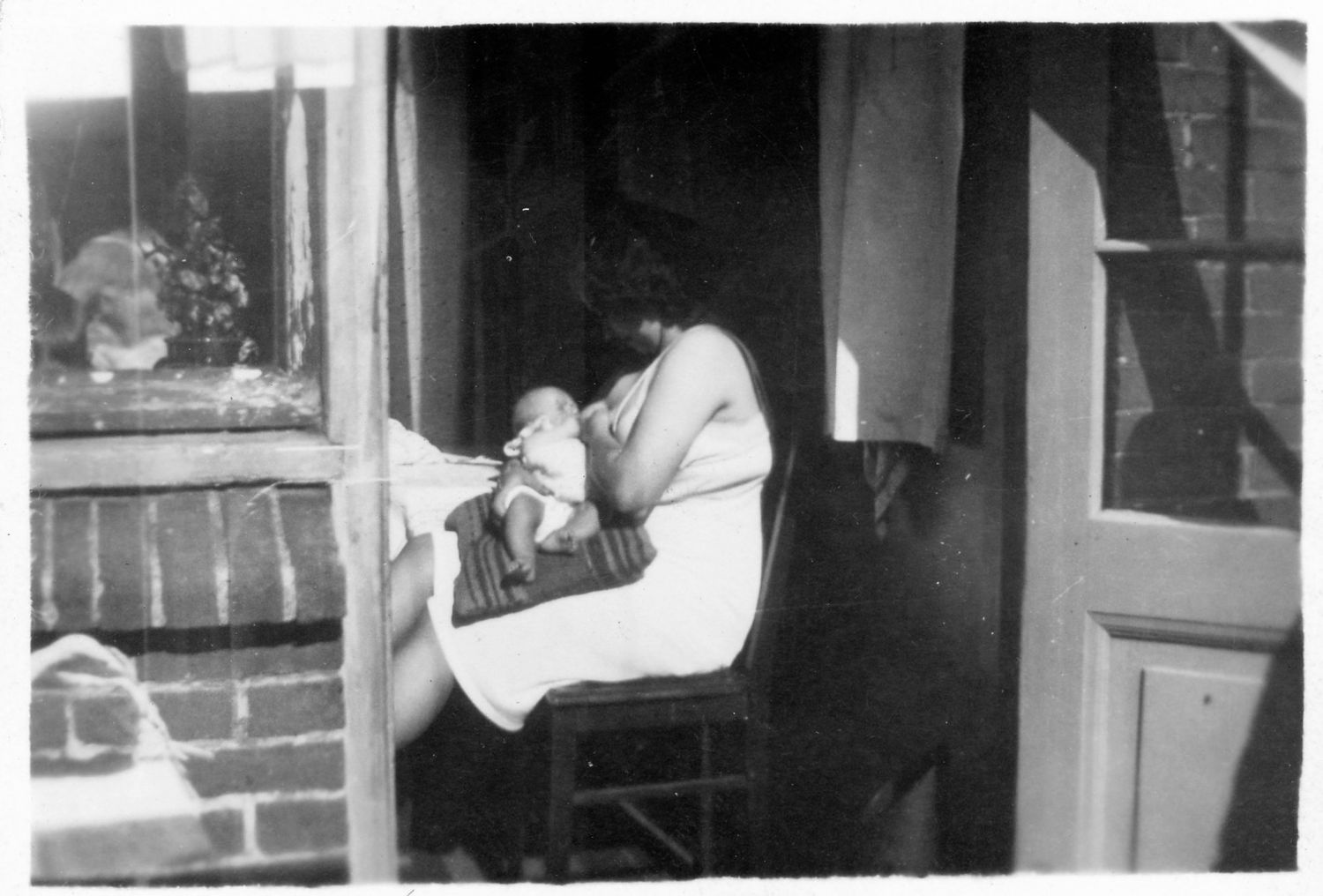 Vintage black and white photo of someone resting on a porch near a window.