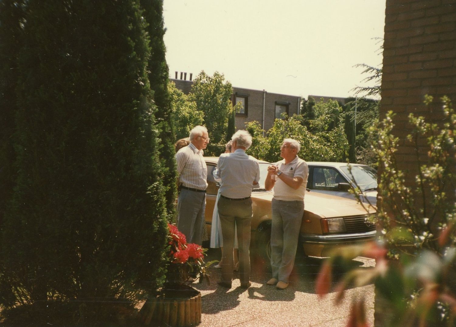 Color photograph from the 1970s showing a group gathered near a car in a driveway.