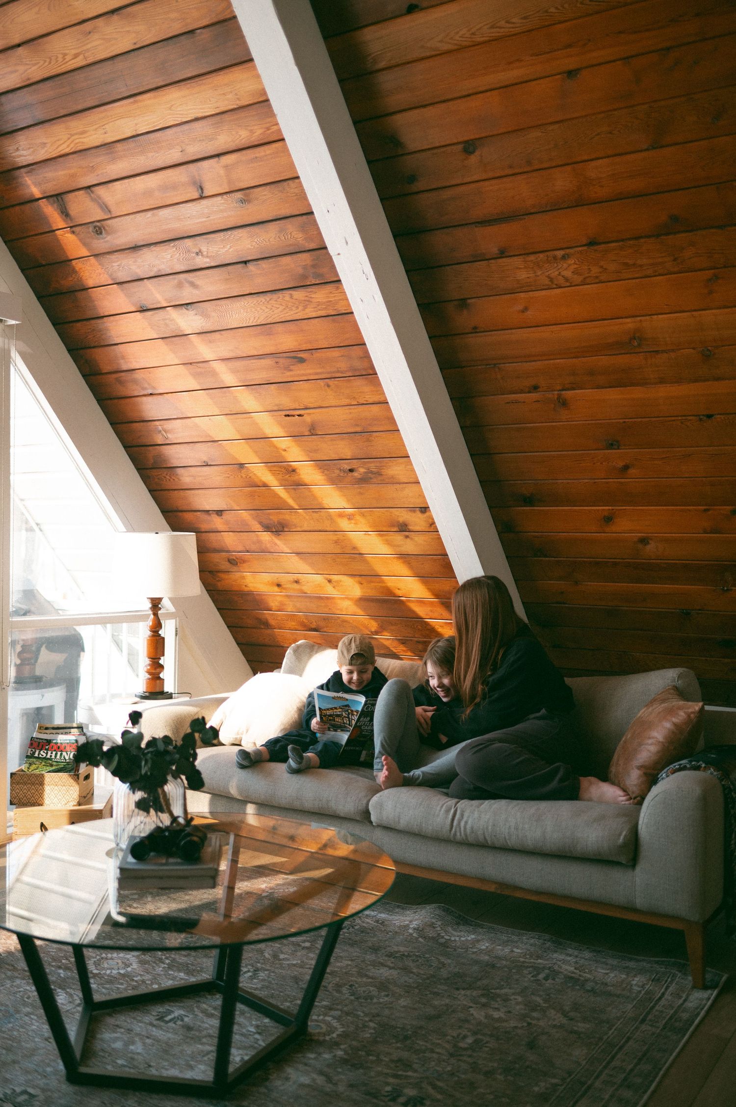 Cozy attic living room with wooden panel ceiling and gray sofa beneath sloped wall near geometric coffee table.