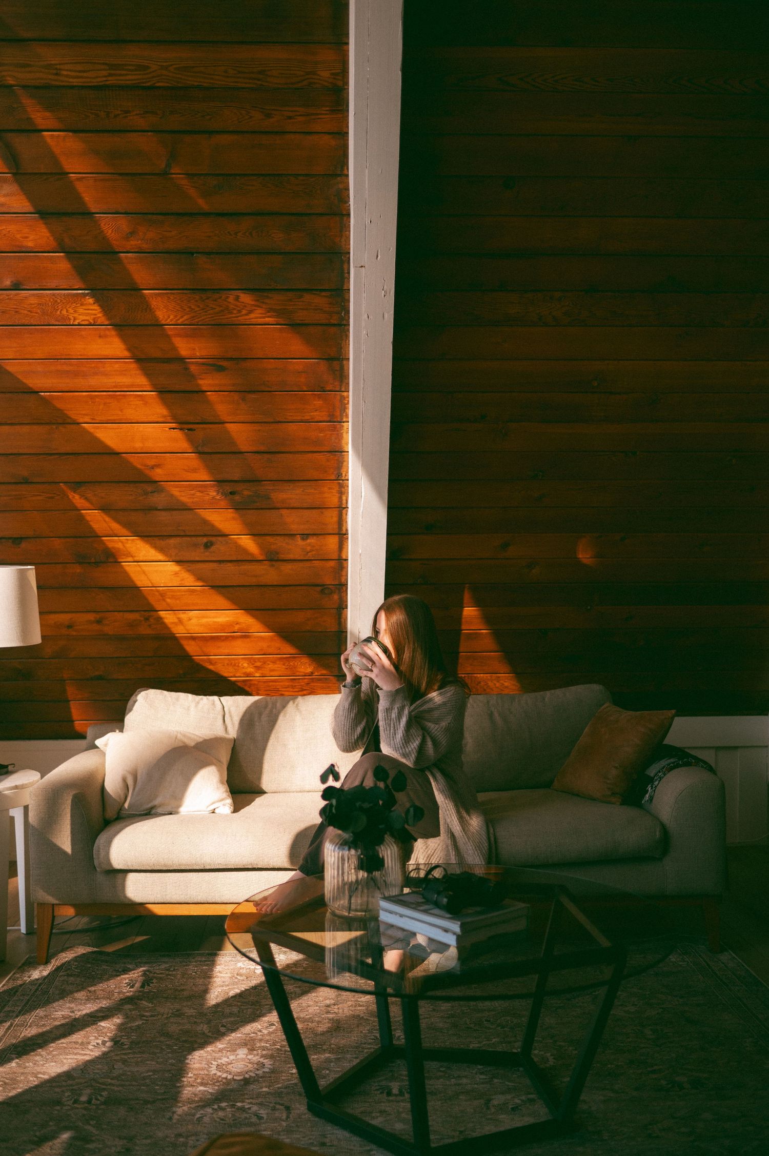 Cozy living room scene with dramatic sunlight streaming through wooden blinds onto a white couch during golden hour.