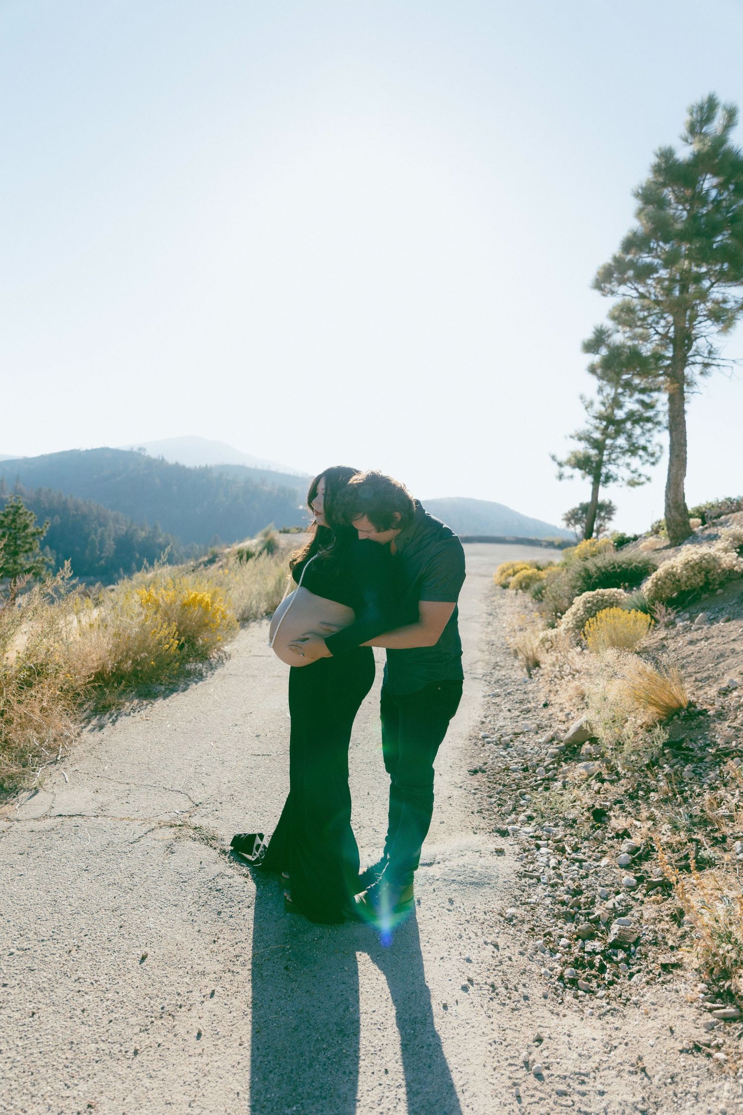 A graceful maternity portrait under a willow tree featuring a flowing polka dot dress and a small child in nature.