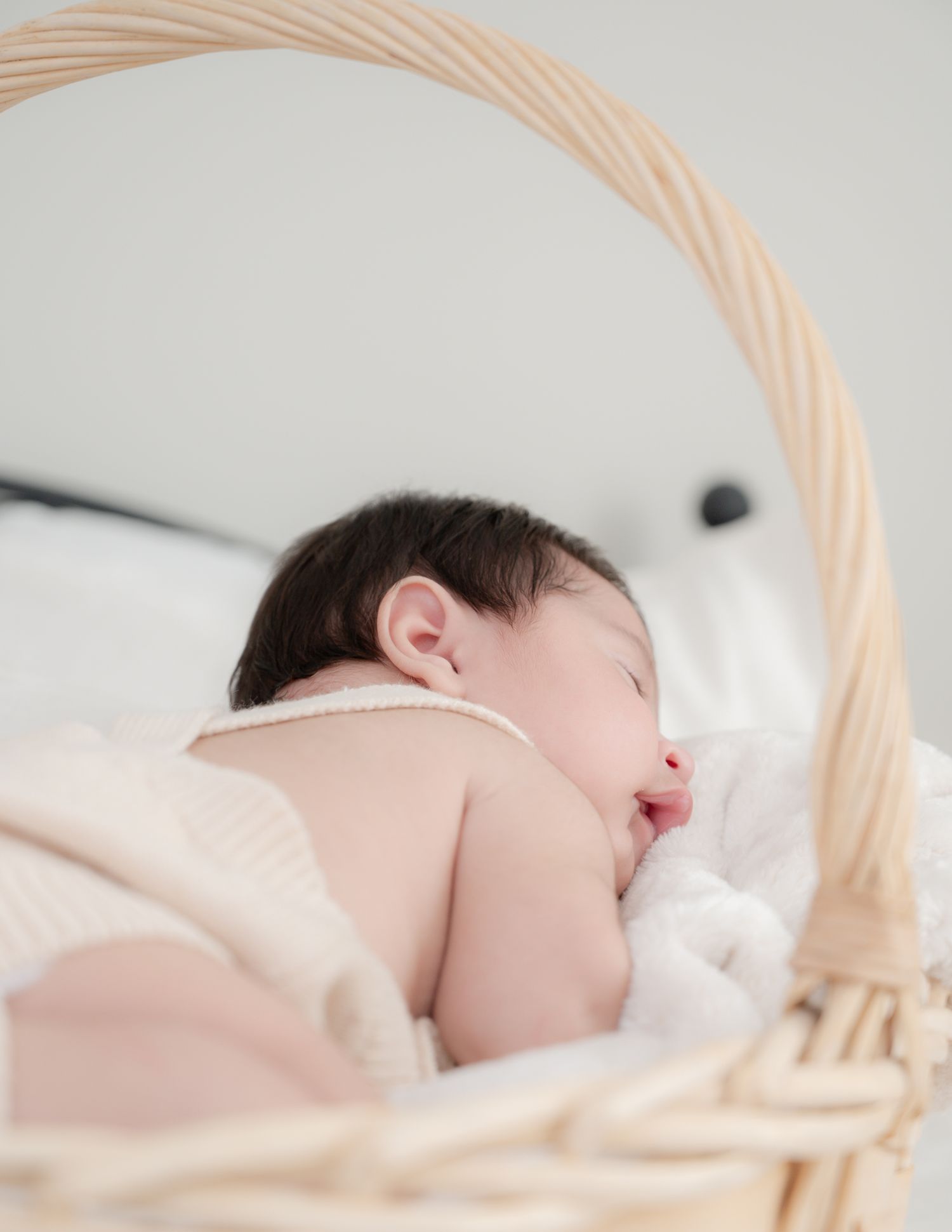 Baby sleeping peacefully in woven basket with soft white bedding.