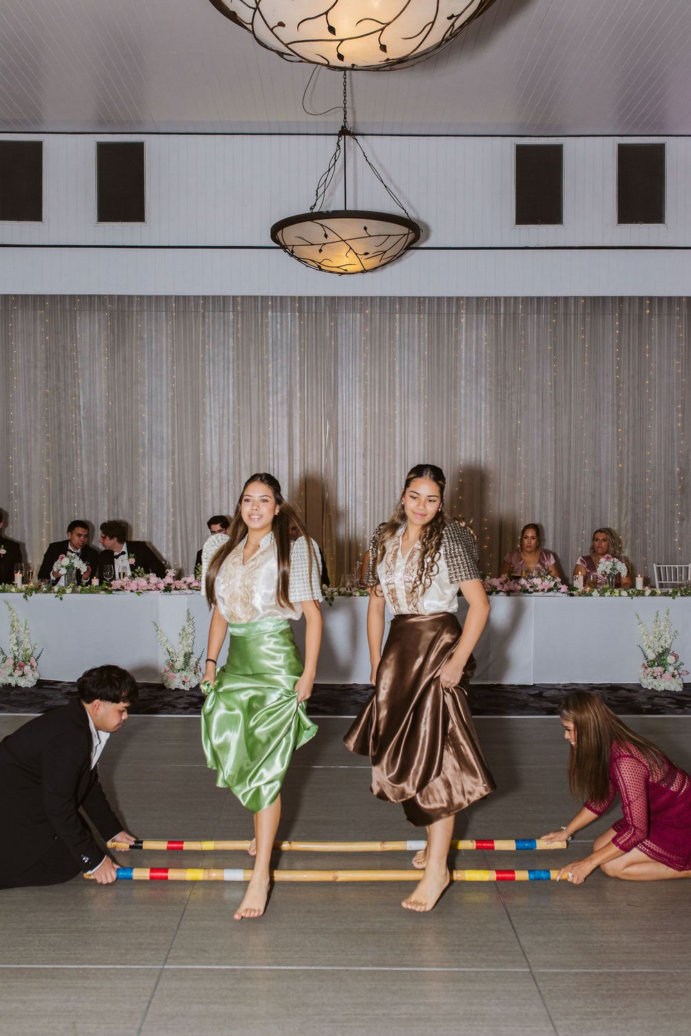 Creative wedding photo of attendees sitting along a wall with colorful dresses.