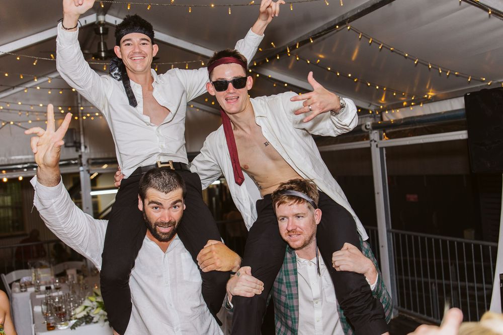 Group of wedding guests celebrating joyfully under string lights at reception.