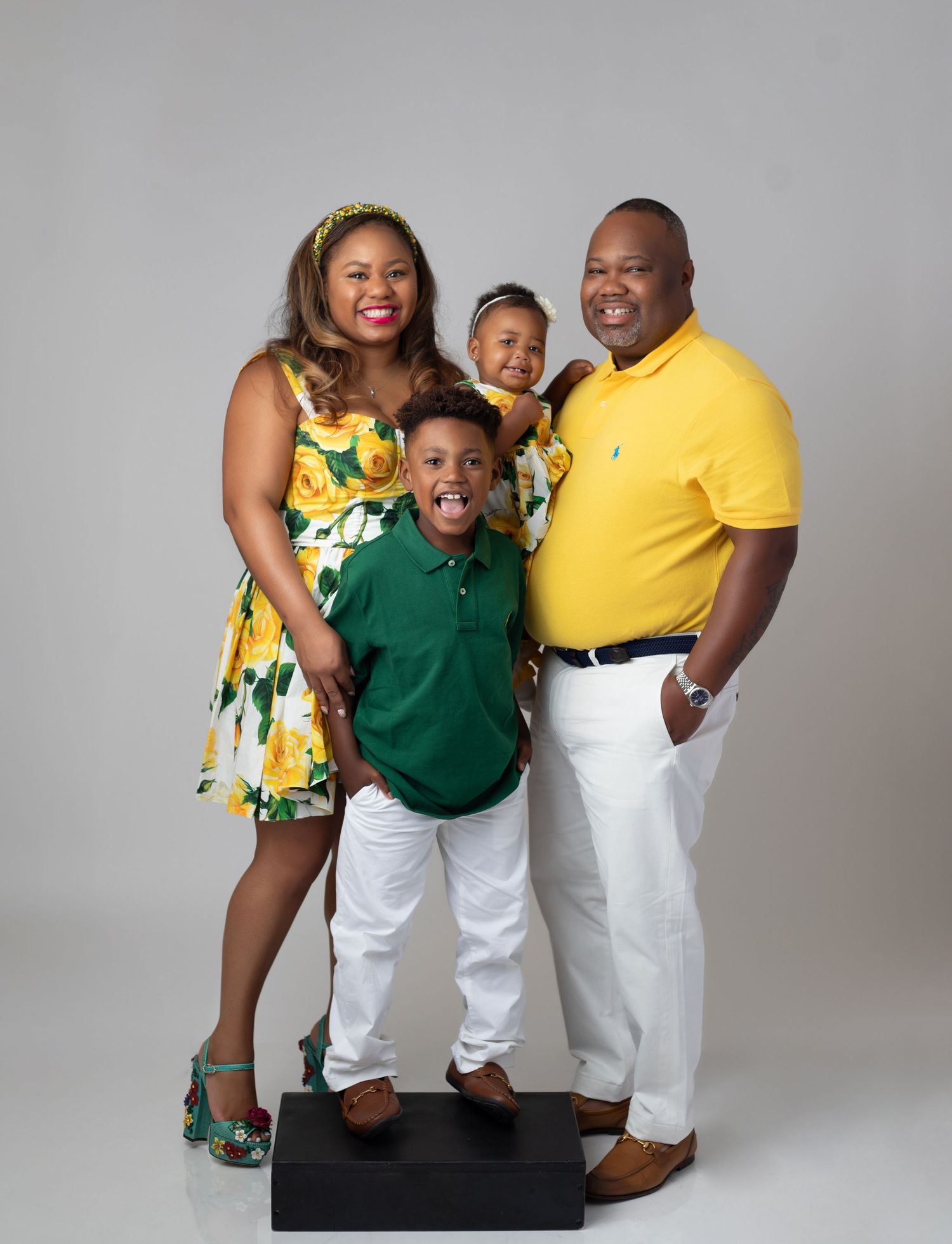 A beautiful family of four poses together against a gray backdrop wearing coordinated yellow, green and white outfits.