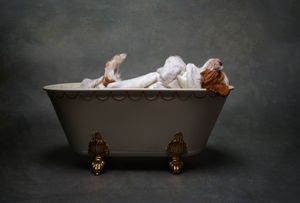 Vintage white porcelain clawfoot bathtub with ornate gold feet displayed in dramatic lighting against dark background.