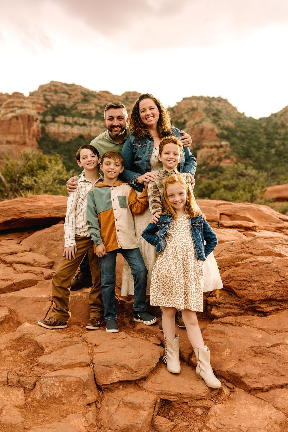 Family of six smiling together on red rocks with Sedona Arizona sandstone buttes behind them.