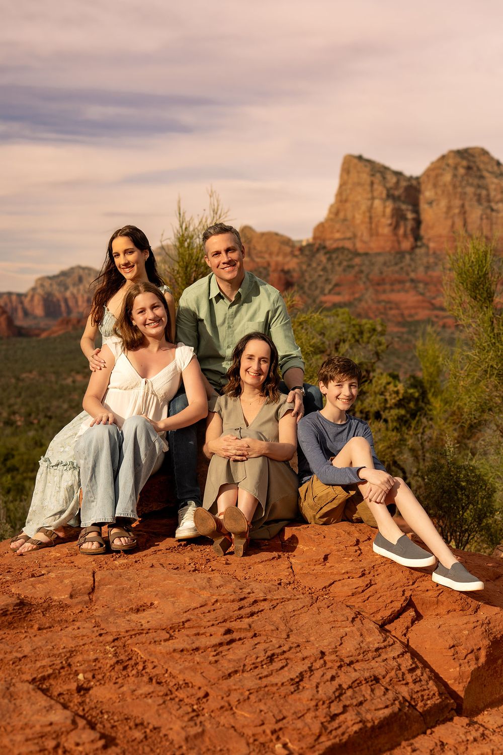 Family of five posing on red rocks in Sedona Arizona with stunning red rock formations in background.