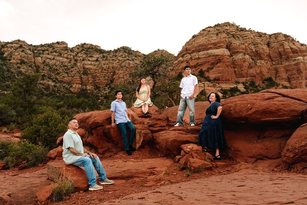 A family of five poses on red rock boulders in Sedona, Arizona, with layered red cliffs in background.