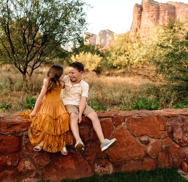 Children sharing a laugh while sitting on rustic stone wall with Sedona desert landscape behind them.
