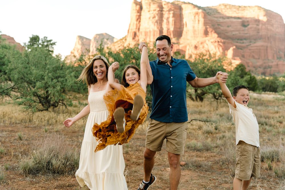 Happy family of four joyfully playing in a scenic desert landscape with red rock formations in Sedona, Arizona.