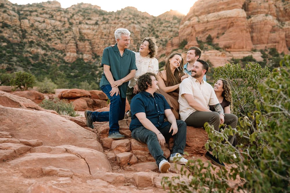 Group of eight people posing on red rock formations in Sedona, Arizona, surrounded by desert shrubs and sandstone cliffs.