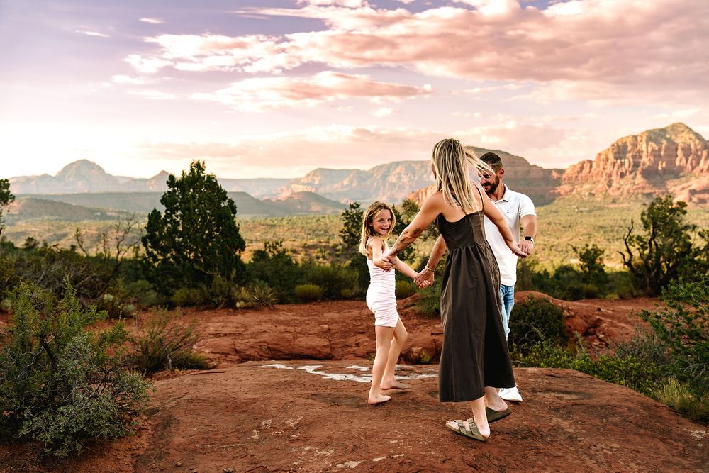 Joyful family dancing and playing together on red rock overlook with panoramic Sedona Arizona sunset views.
