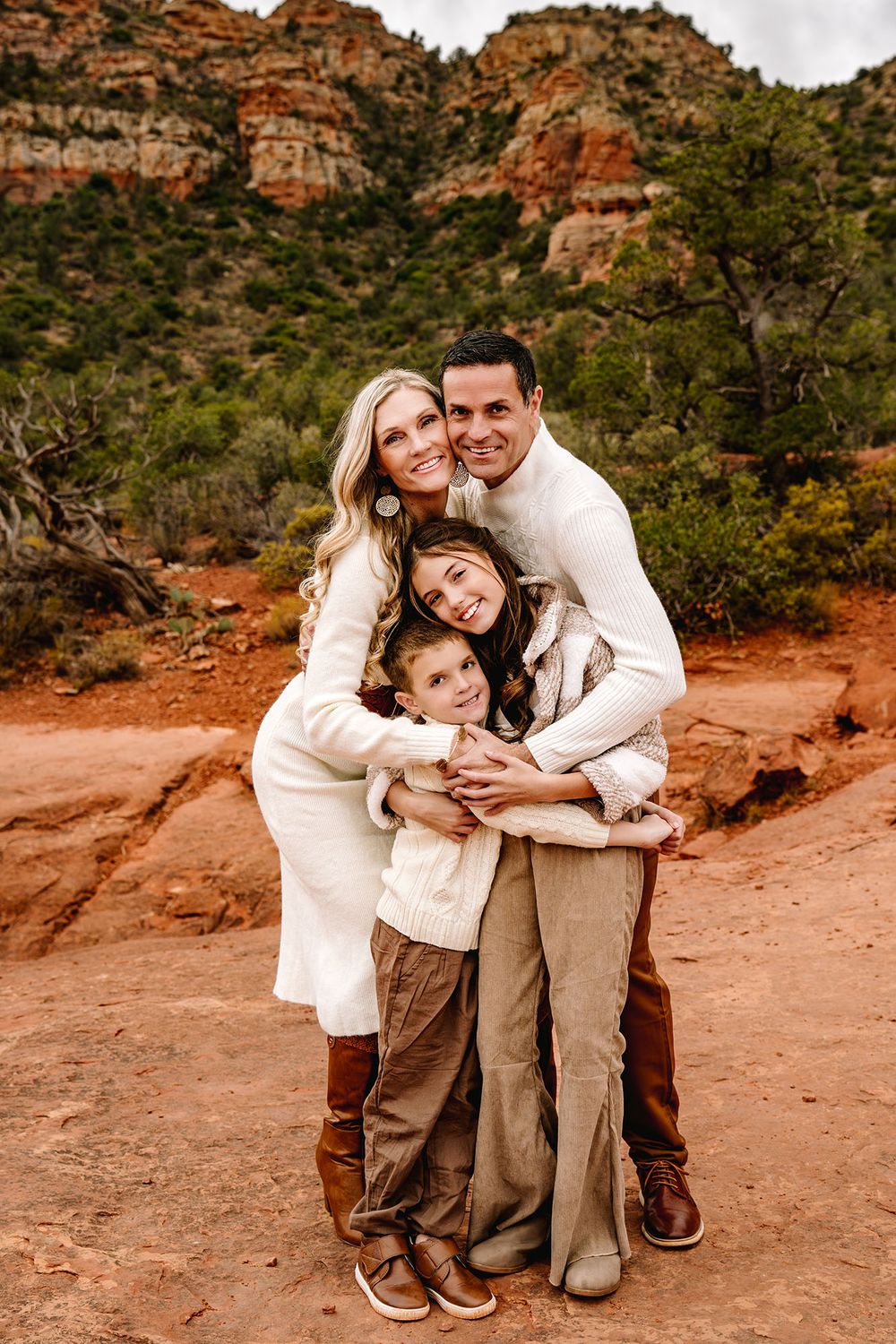 Happy family of four hugging together in Sedona red rock canyon landscape during photo session.