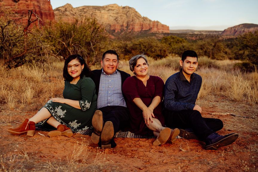 Four people sitting casually on desert ground with towering Sedona red rock formations behind them.
