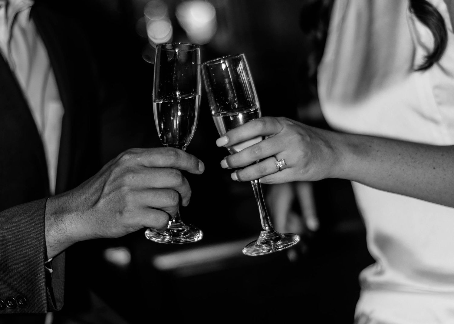 Black and white close-up photo of hands holding champagne glasses during a celebration toast.