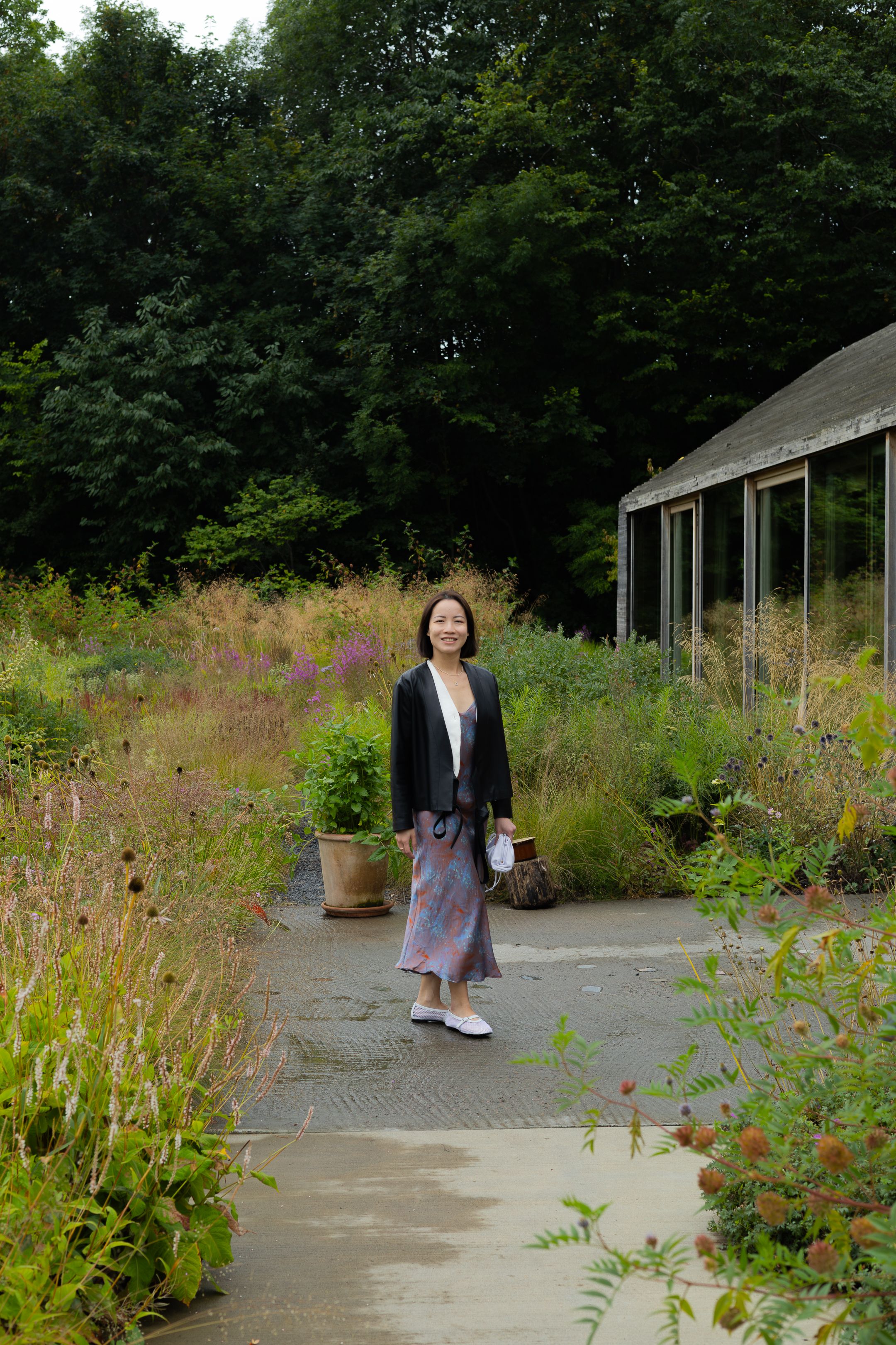 A garden path leads through wildflowers to a modern structure with glass windows and wooden siding.