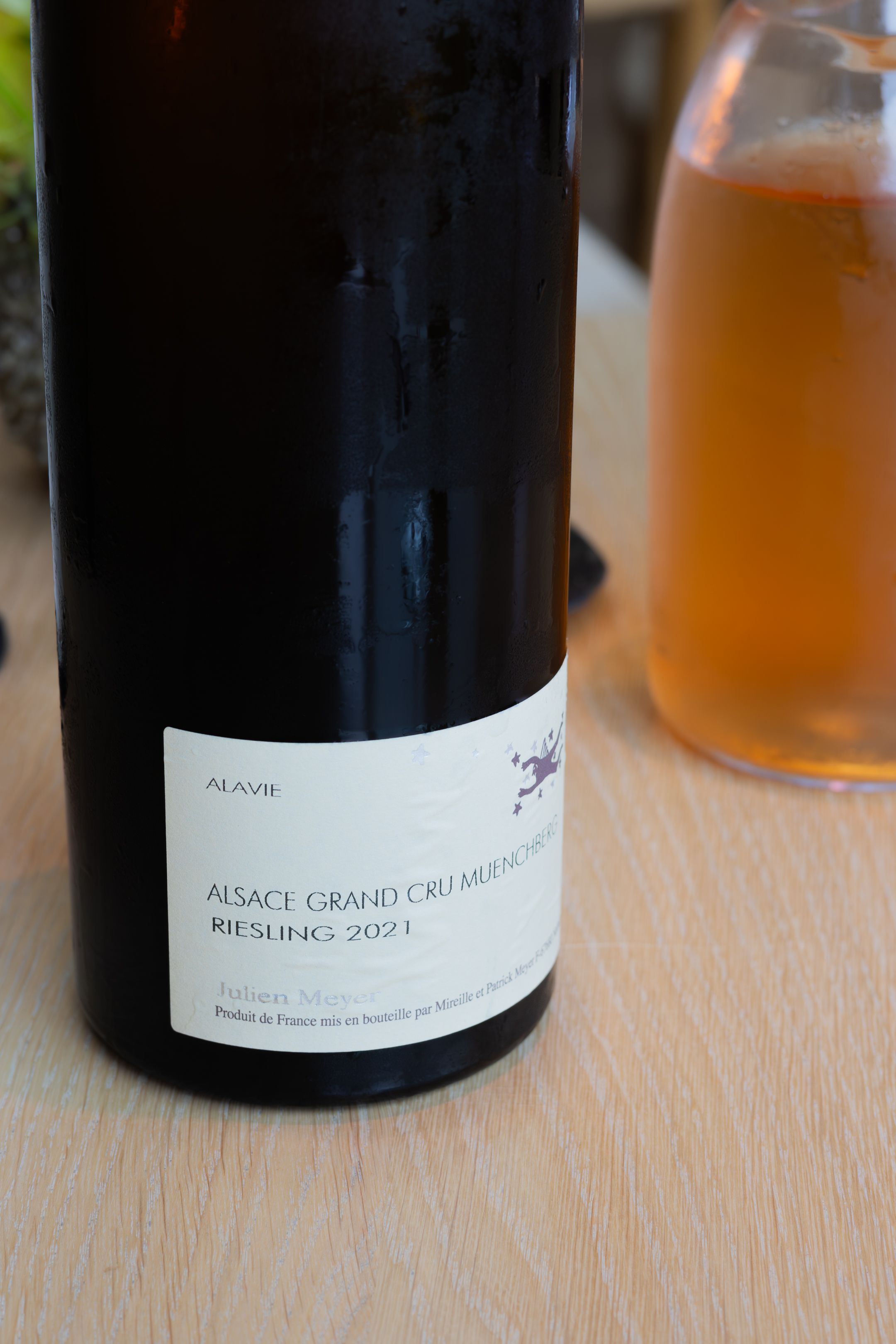 A bottle of Alsace Grand Cru Riesling 2021 wine sits on a wooden table.