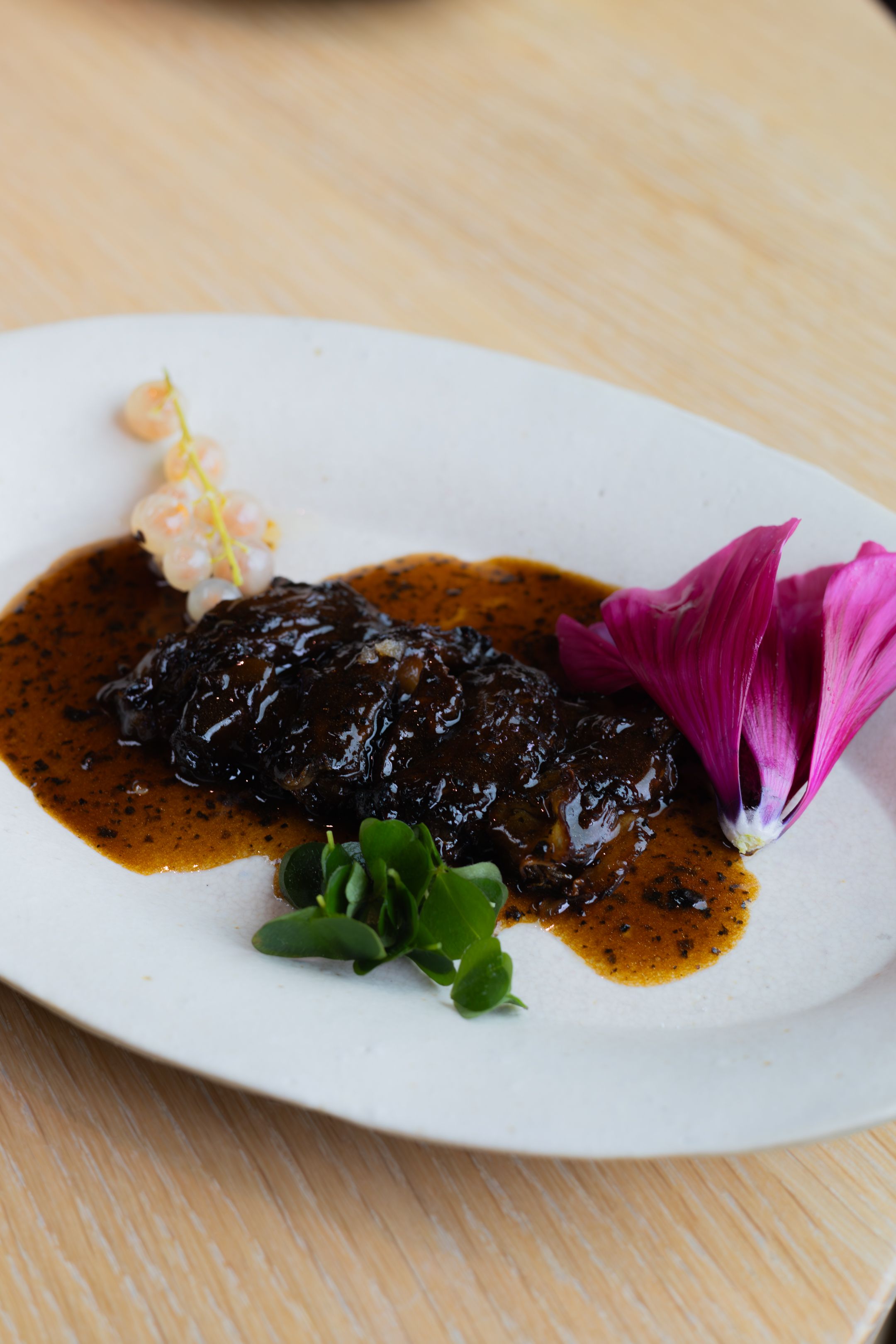 Glazed meat dish with purple flower garnish served on a white plate.