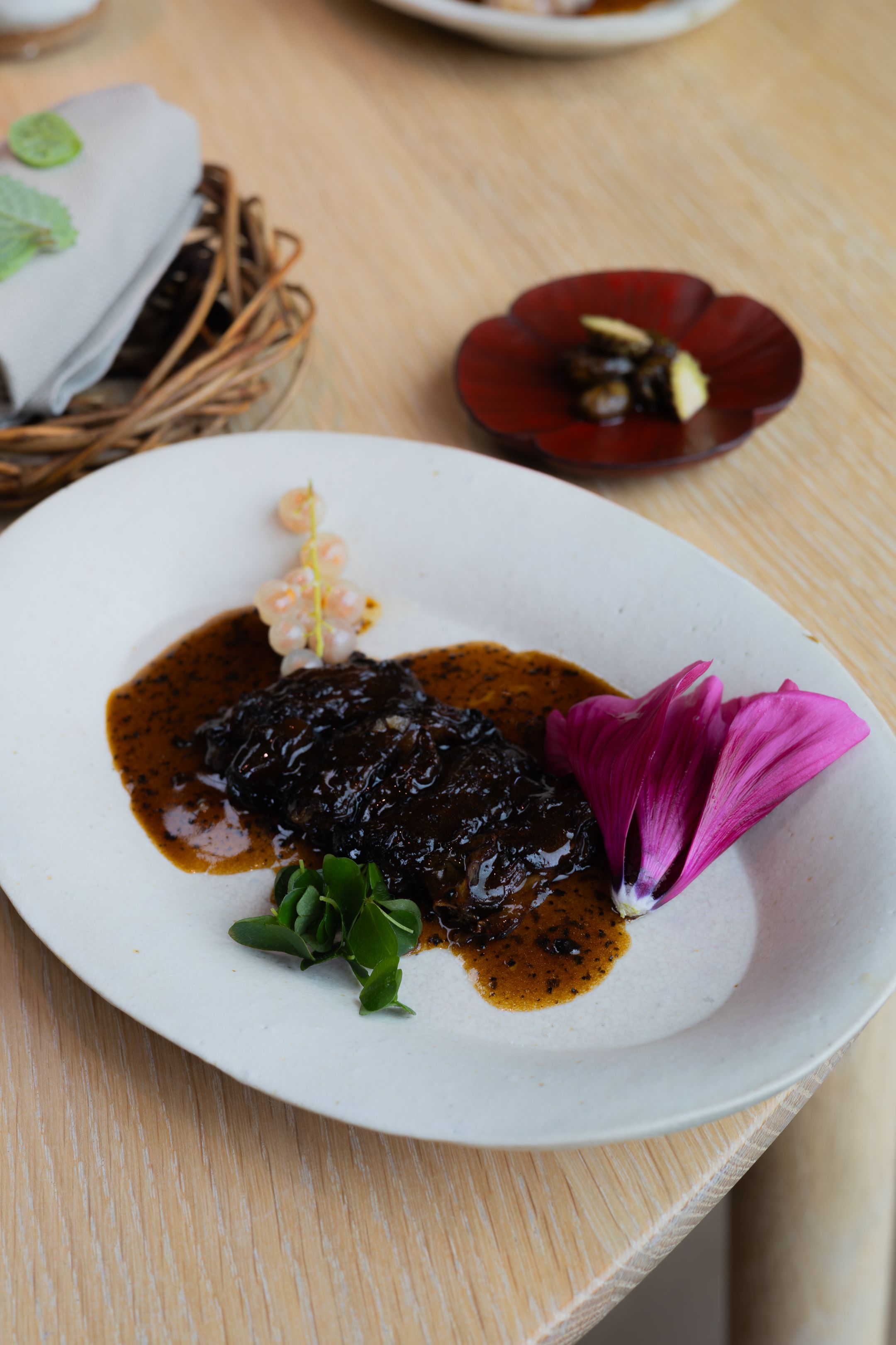 Elegant plated dish with dark sauce and purple flower garnish on wooden table.