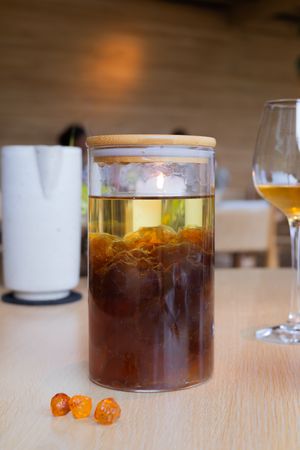 Glass container of layered tea with citrus and wine glass on wooden table.