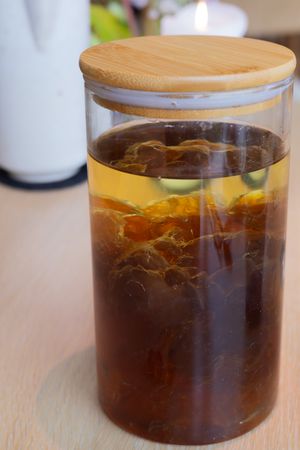 Tall glass jar with wooden lid containing layered tea and citrus.