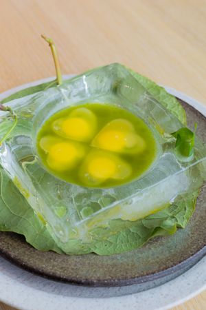 Four yellow spherical garnishes displayed in clear gelatin on lettuce leaves.