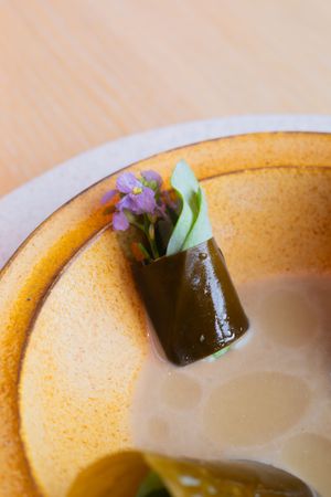 Close-up of pickled vegetable roll garnished with purple flowers in cream sauce.