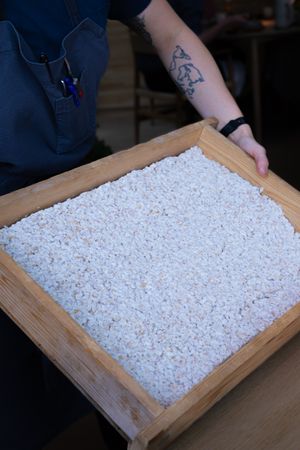 A wooden tray filled with white rice or salt grains shown from above.