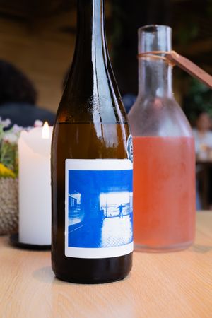 Wine bottle with blue label next to pink beverage in glass bottle.