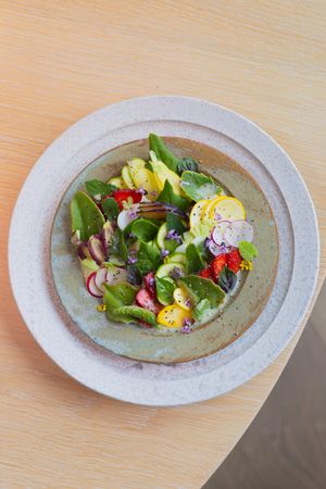 Fresh garden salad with radishes, edible flowers, and greens on a gray ceramic plate.
