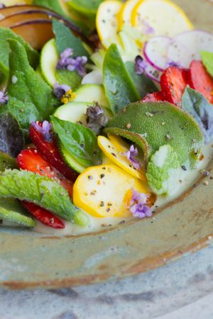 Close-up of garden salad with strawberries, yellow eggs, and purple flowers.