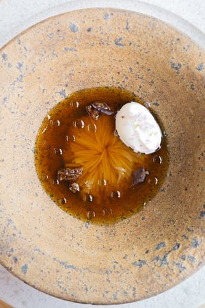 Clear broth with star pattern and white foam garnish in a textured ceramic bowl.