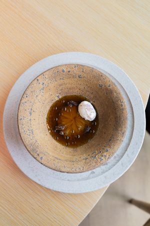 Overhead view of a stone bowl containing amber liquid and white garnish on a wooden surface.