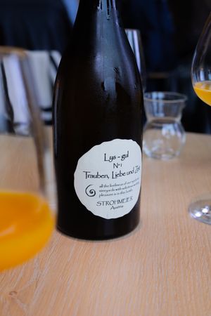 Dark wine bottle with handwritten label on wooden table with glassware.