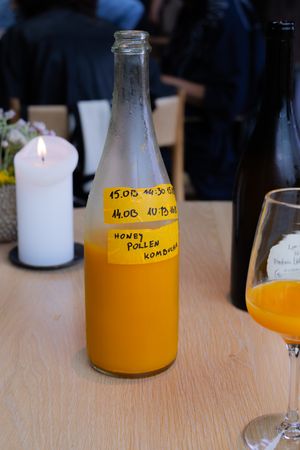 Glass bottle of orange-colored kombucha with handwritten label beside stemware.