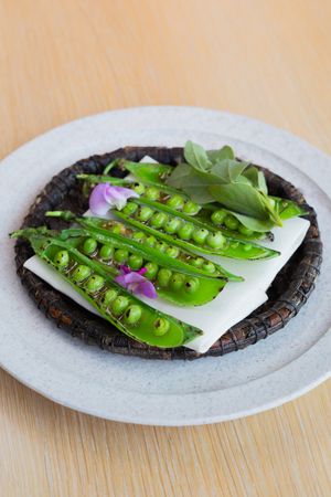 Fresh split pea pods arranged with purple flowers on a dark circular plate.