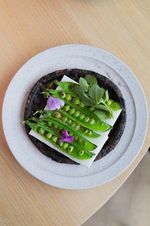Aerial view of fresh pea pods and edible flowers arranged on dark circular base.