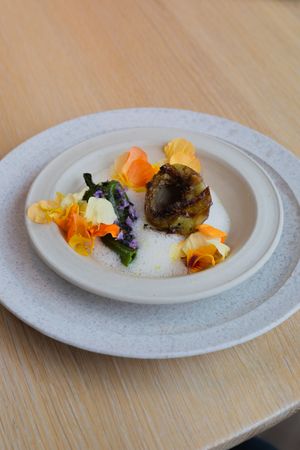 Artfully plated dish with colorful edible flowers and garnishes on white ceramic plate.