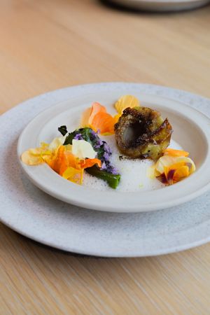 Modern plated dish featuring orange and yellow elements with a dark centerpiece on white ceramic.