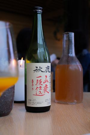 Japanese sake bottle with traditional characters displayed on wooden table with other beverages.
