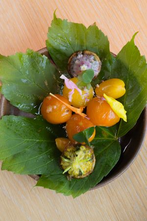 Fresh cherry tomatoes and garnishes arranged on green vine leaves in a dark bowl.