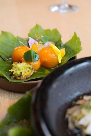 Fresh kumquats and yellow flowers arranged on green leaves beside a black cooking vessel.