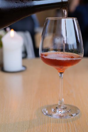 Rose-colored wine being poured into an elegant stemmed glass on wooden surface.
